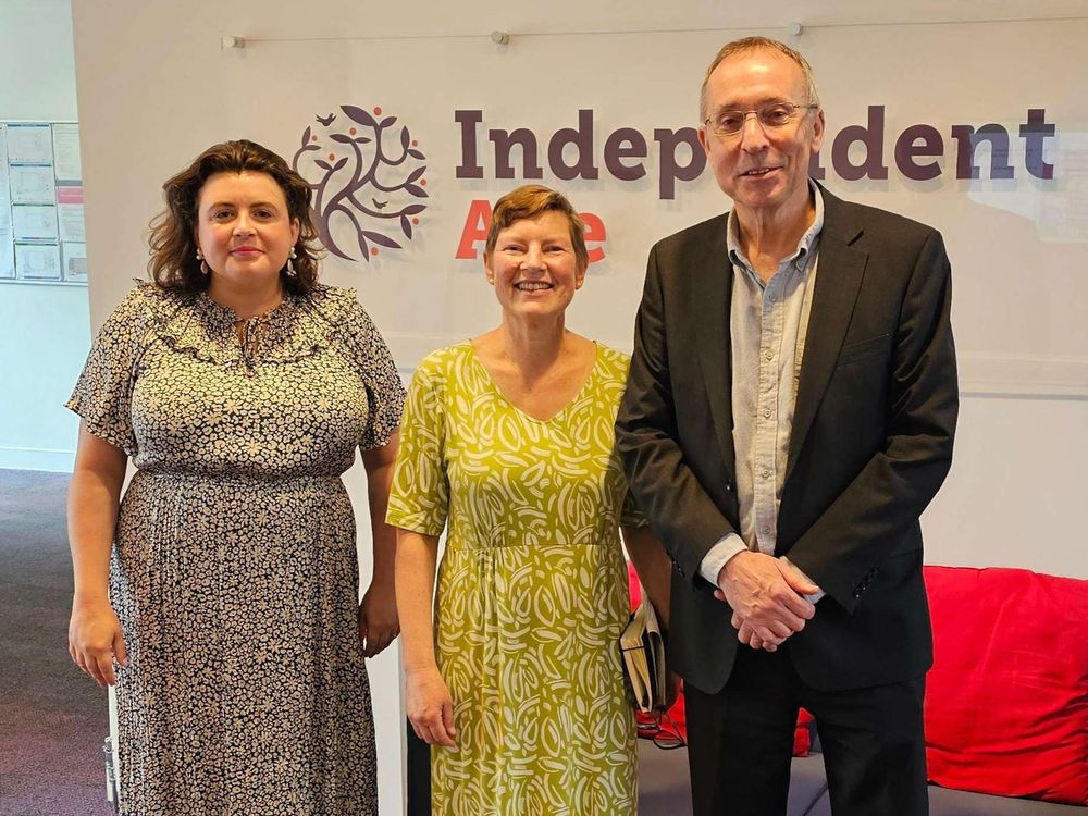 Two women and a man stand in the Independent Age office. They smile at the camera.