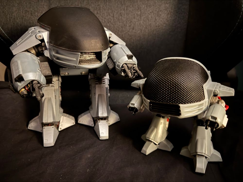 A photo of two toys of the robot ED-209 from the Robocop films; a large detailed one on the left and a smaller simplified version on the right.