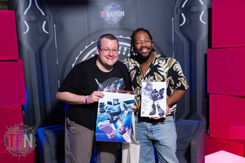 A photo of me standing with Transformers One Jazz voice actor Evan Michael Lee, we’re not holding pieces of Jazz art he’s signed for me.
