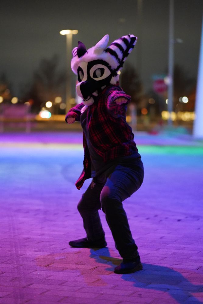 Fursuiter posing on multi-colored illuminated street. 