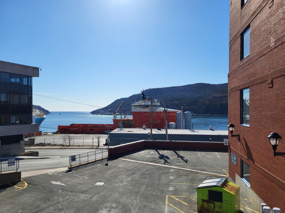 Looking out from a parking lot, a single boat sits in the harbour in front of the narrows in the distance. 