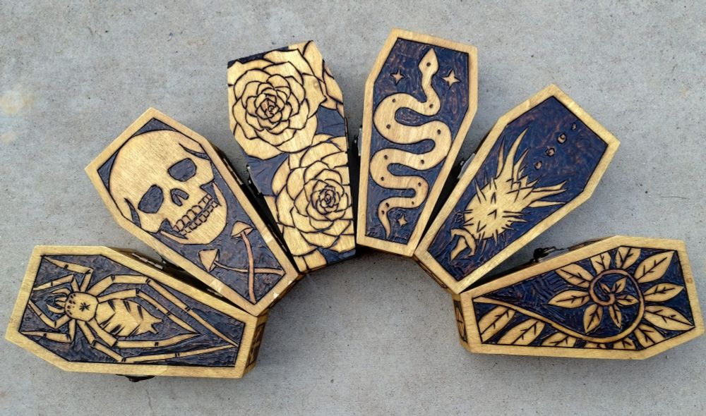 6 mini wood coffin shaped boxes with pyrography designs. A spider, skull, roses,  snake, datura pod, and fern.
