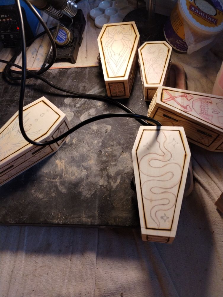 Several wood coffin boxes with penciled in designs waiting to be wood burned.