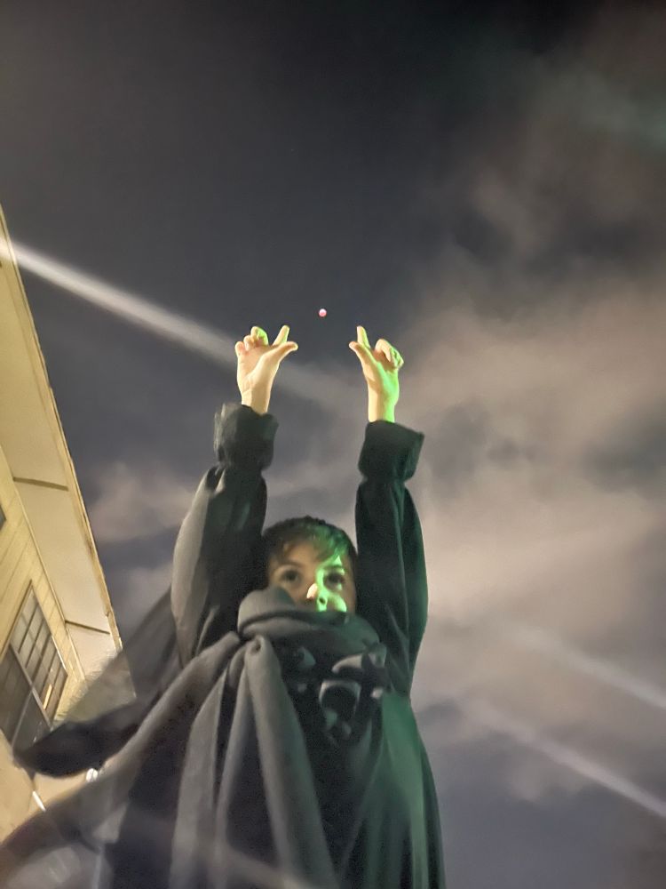Boy dressed all in black with hands in the air, the moon positioned between his hands during the March 13/14 lunar eclipse