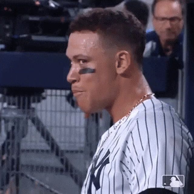 a baseball player wearing a ny yankees jersey looks to his left .