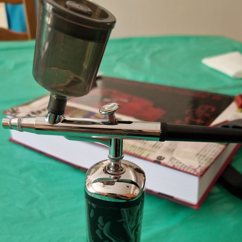 Photo avec un aerographe au premier plan et un grand livre derrière qui attend d'être peint.