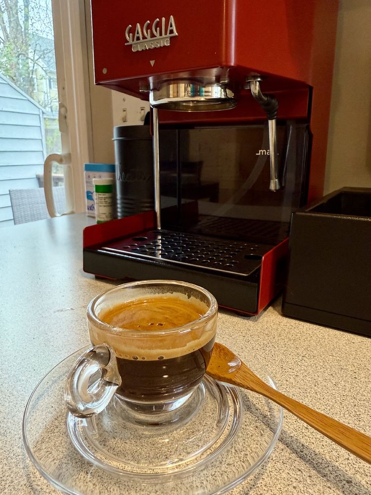 Espresso in a glass cup & saucer in front of a red Gaggia Classic. 