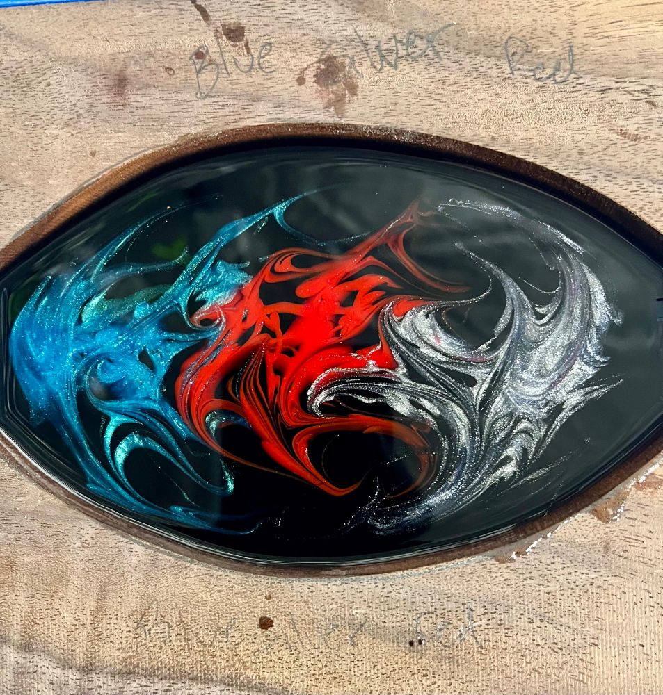 Walnut dice box top with a large oval cutout filled with black epoxy and wispy turquoise red and silver slashes in the center 