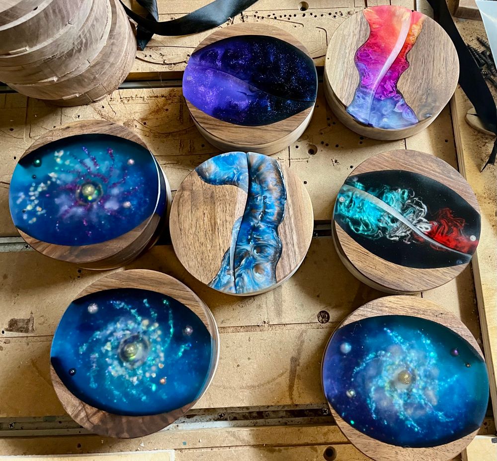 Seven round dice boxes made from walnut and epoxy. The epoxy incorporated into the top looks like spiral galaxies and understand colors in between.