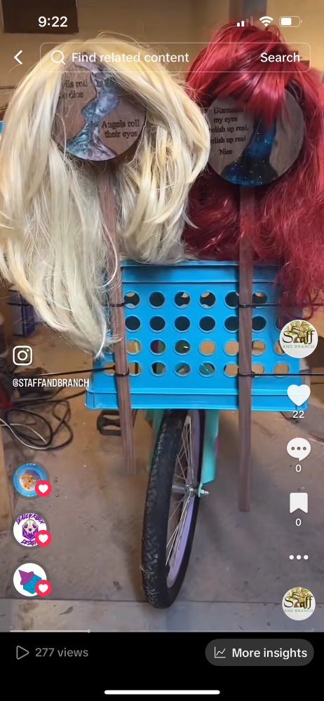 Dice box with a quote from Taylor Swift’s album Midnights wearing a bright red wig and A different Taylor Sift dice box are tied to stakes and strapped to the front of a bicycle.