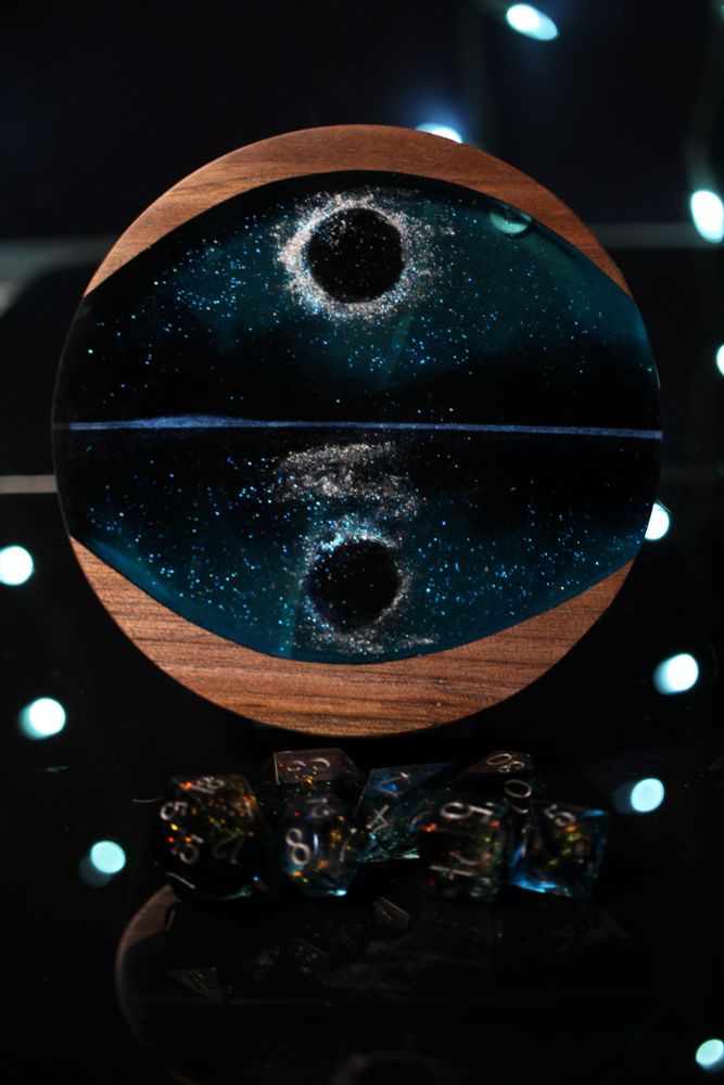 Round walnut dice box with a large oval cut out filled with blue and black epoxy that looks like an eclipse reflected in a lake.