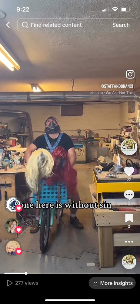 Dice box with a quote from Taylor Swift’s album Midnights wearing a bright red wig and A different Taylor Sift dice box are tied to stakes and strapped to the front of a bicycle. Bicycle is being riden by a guy in a mask laughing