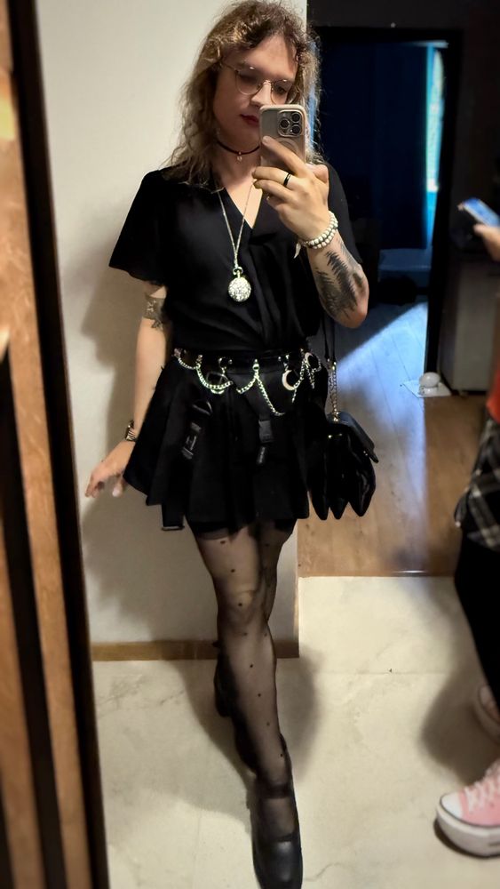 Ines in dotted tights, black Dr Martens high heels, a tactical skirt and a belt with silver chains and moons on it, a lace black shirt, and with a pocketwatch hanging from her neck. She is incredibly hot :3