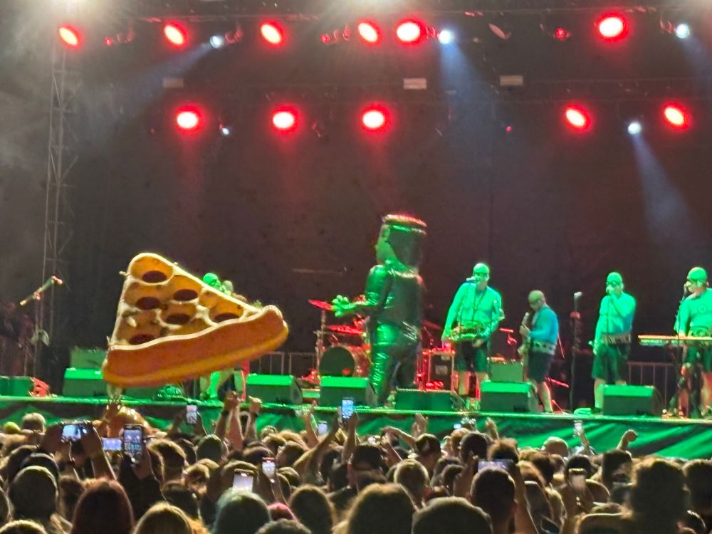 The ska band The Aquabats playing on stage while battling an inflatable Frankenstein’s monster. An inflatable pizza bounces across the audience