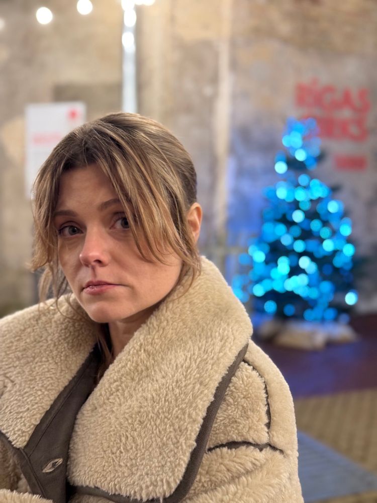 A photograph of a woman standing in a courtyard in front of a lit Christmas tree.