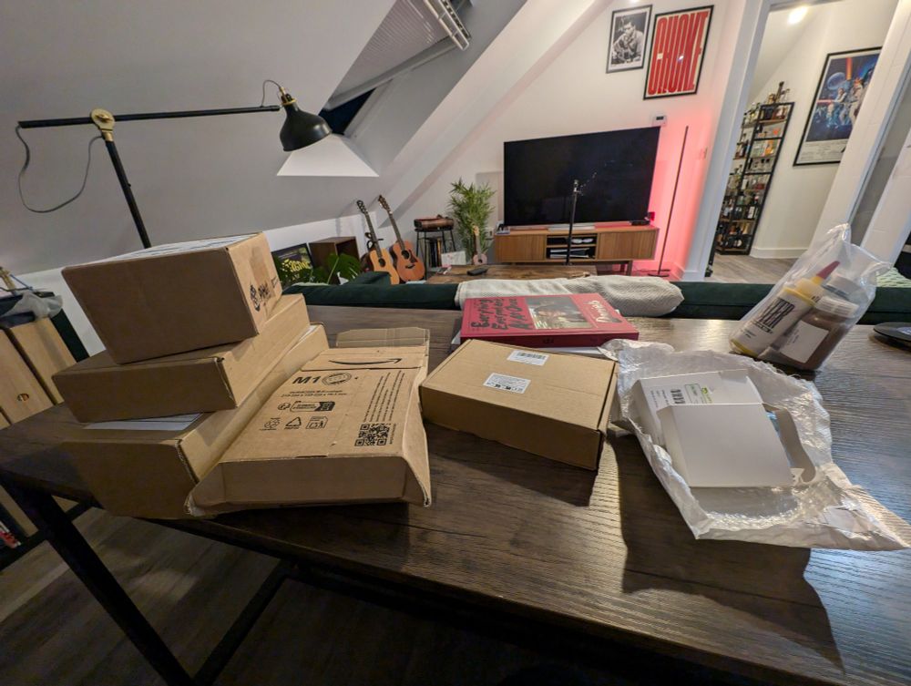 A table in a living room covered in unopened packages containing parts for a robot. 