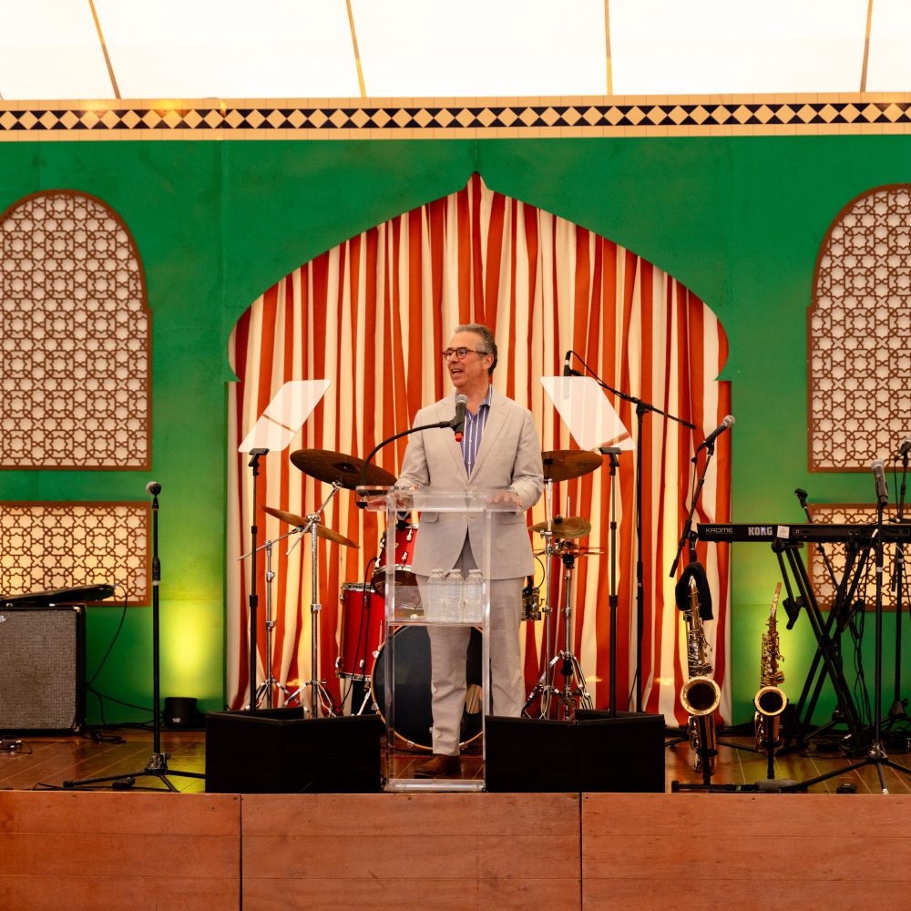 Person speaking on a stage decorated with striped red and white backdrop and green arches.