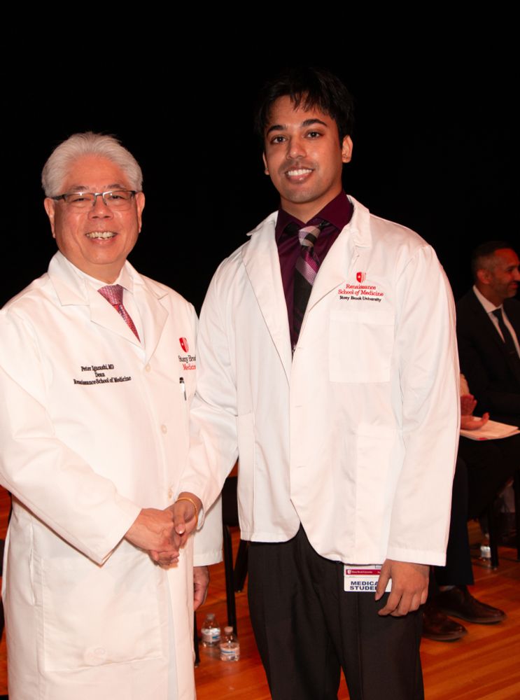 Two individuals in white lab coats with the Stony Brook University Renaissance School of Medicine logo standing side by side, smiling. 