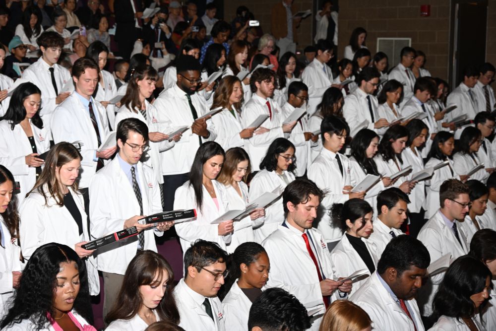 Group of medical students wearing white coats at a ceremony, reciting an oath.