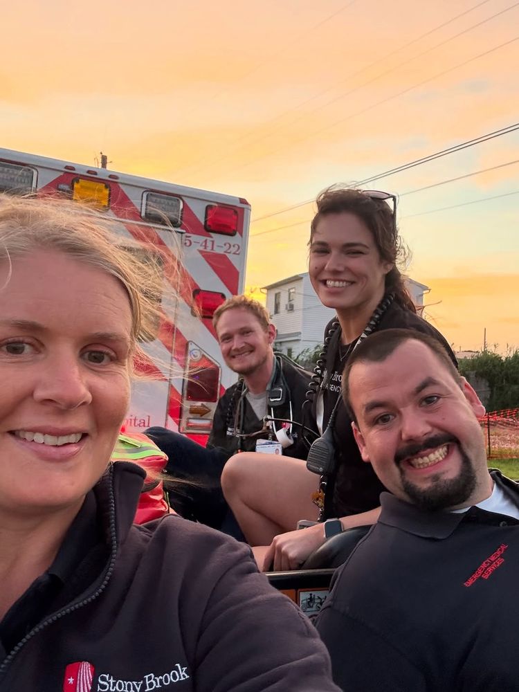 Four emergency responders, posing in front of a Stony Brook Medicine ambulance during sunset.