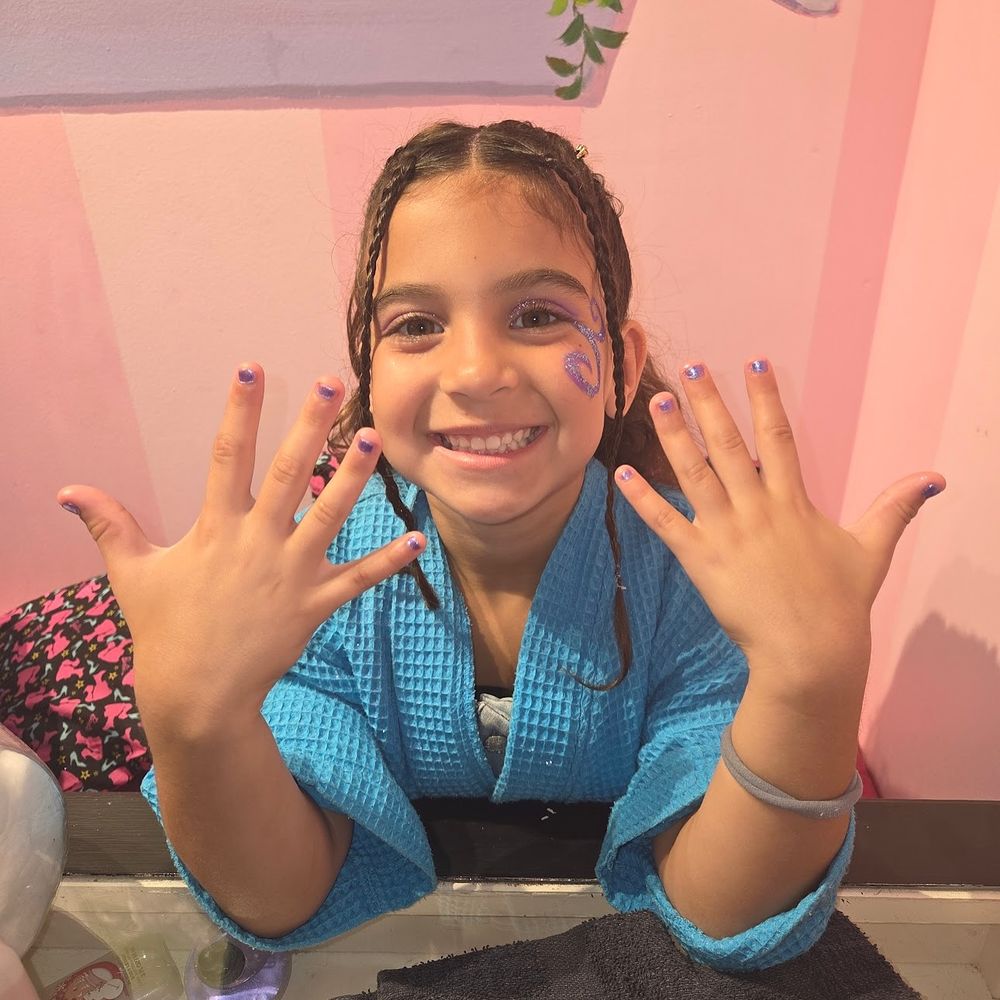 A child smiling and showing off freshly painted nails and a face painting of a butterfly.