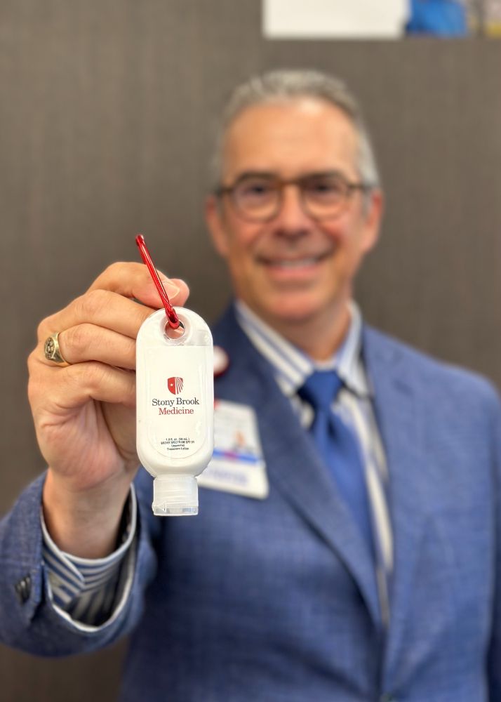 Person in a blue suit displaying a Stony Brook Medicine sunscreen bottle.