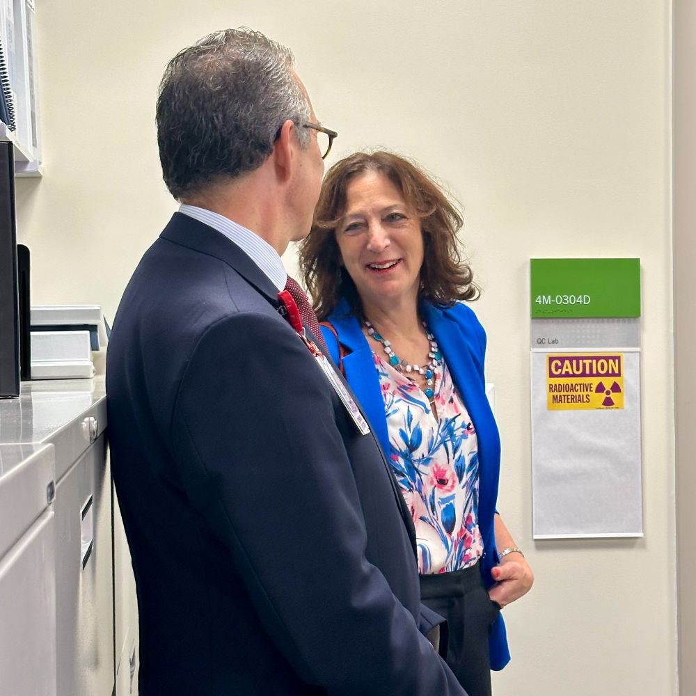 Two professionals are engaged in conversation next to a sign labeled "Caution Radioactive Materials" in a lab setting.