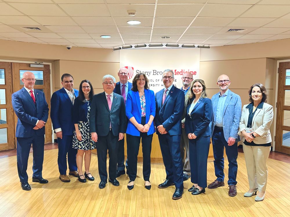 Group of nine professionals posing in front of a wall that says Stony Brook Medicine.