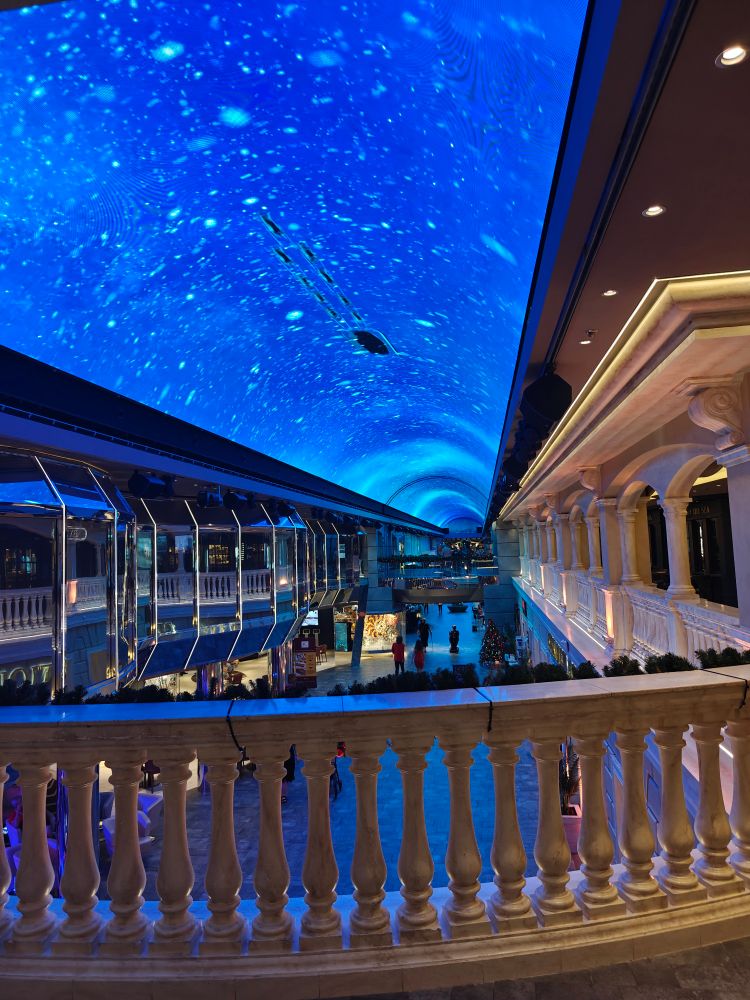 A view of the indoor promenade facing astern from the upper floor. The video on the LED ceiling is a gentle snowfall with an animated sleigh and reindeer team.