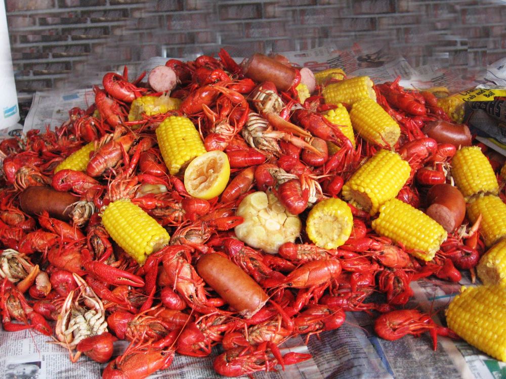 A pile of boiled crawfish with garlic, corn on the cob, and sausage on newspaper