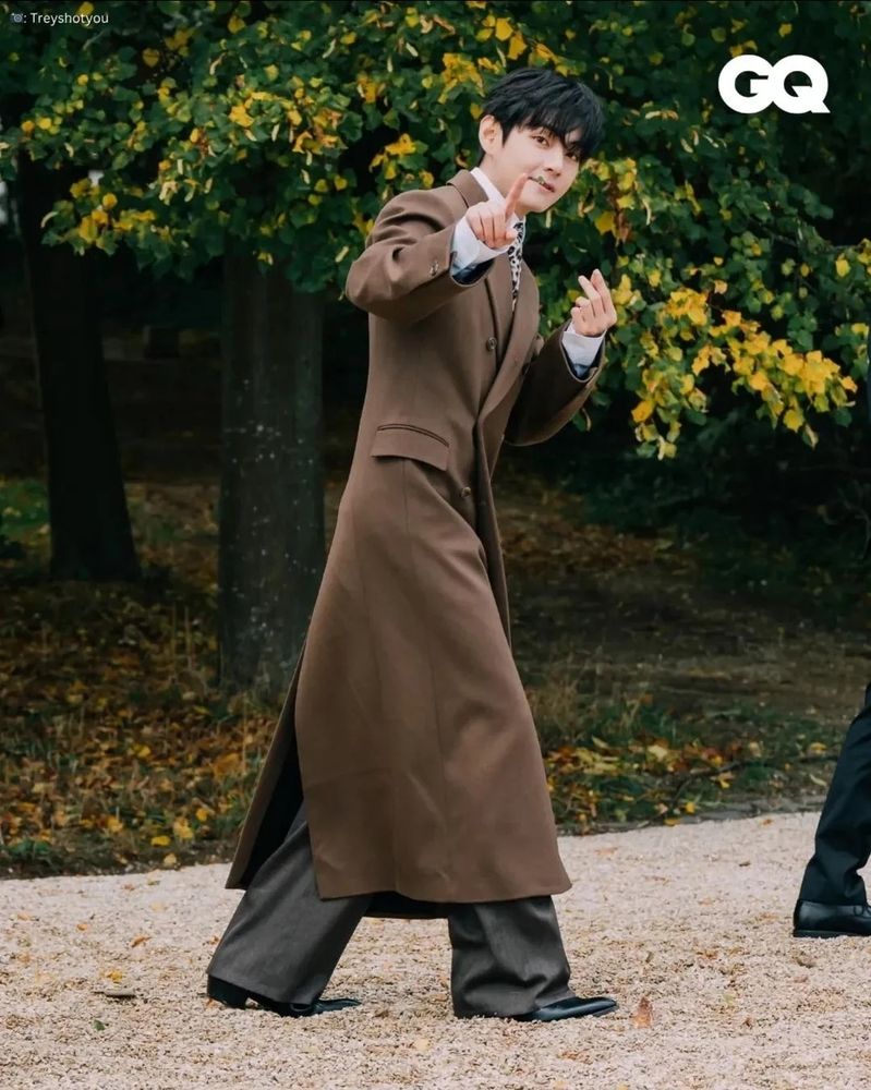 Kim taehyung in a long brown coat that almosz reaches hins ankles. 
He's also wearing charcoal grey wide legged trousers and a white Shirt.
Tldr: he's a lot more dressed than jimin.