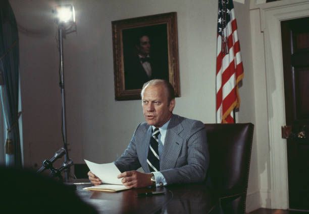President Gerald Ford delivers remarks seated at his desk.