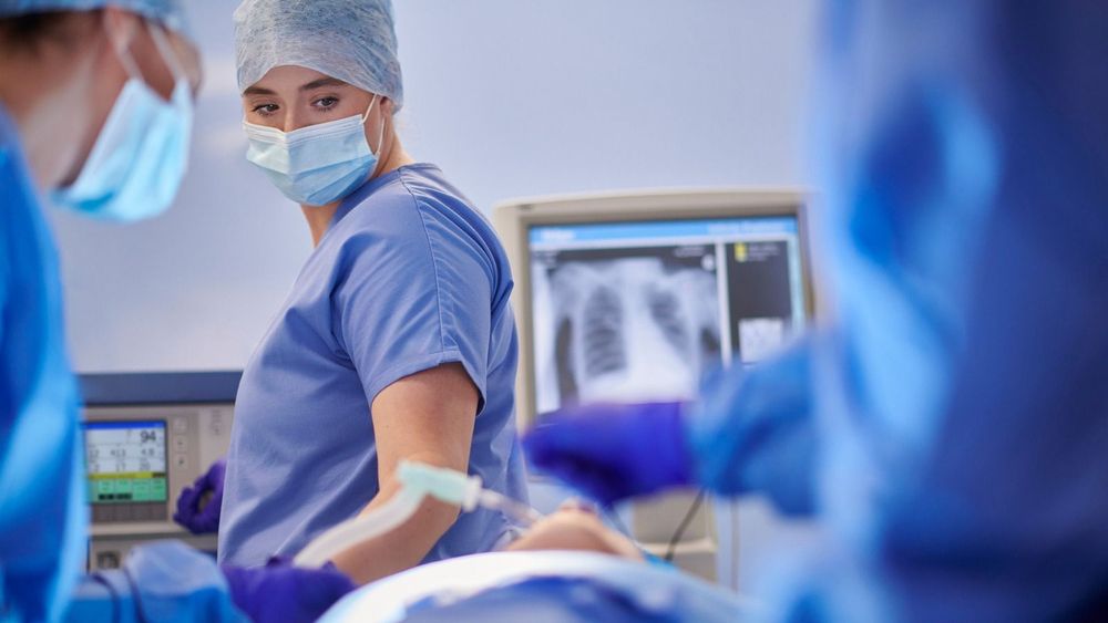 A group of doctors stood around an intubated patient. There is an x-ray of a chest behind them