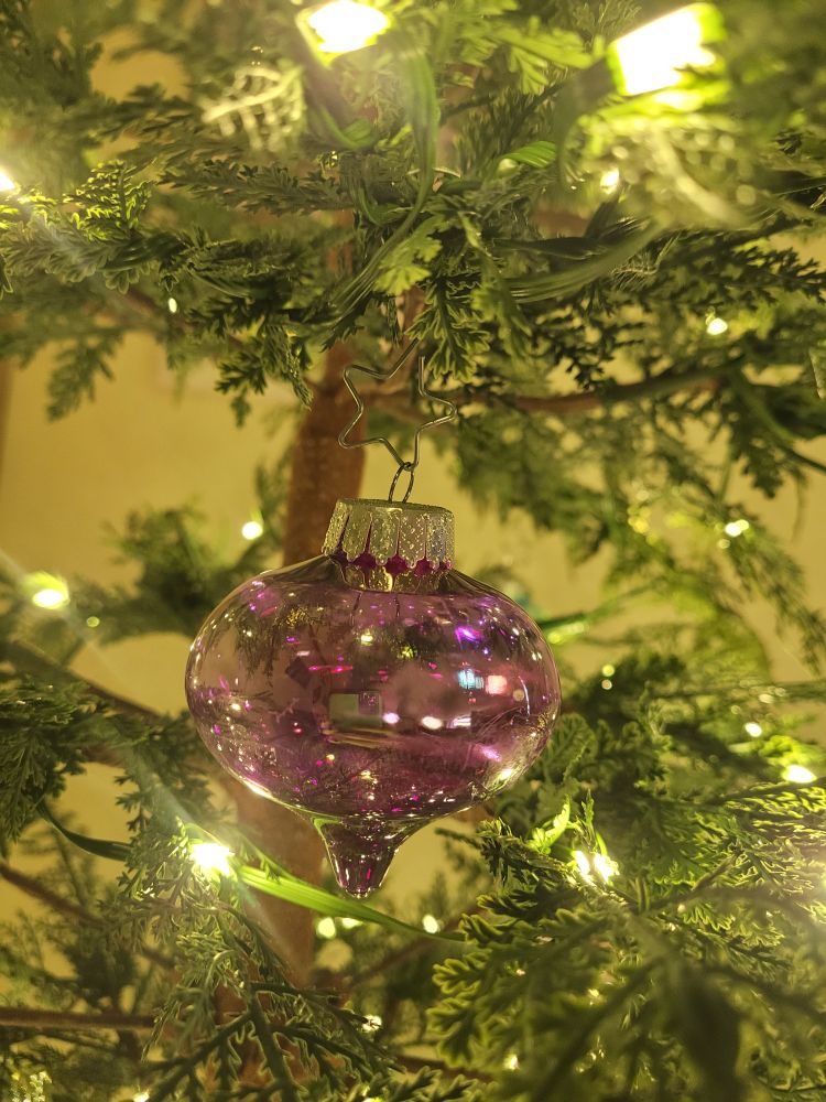 Closeup of a clear purple ornament hanging from a star shaped hook on a christmas tree