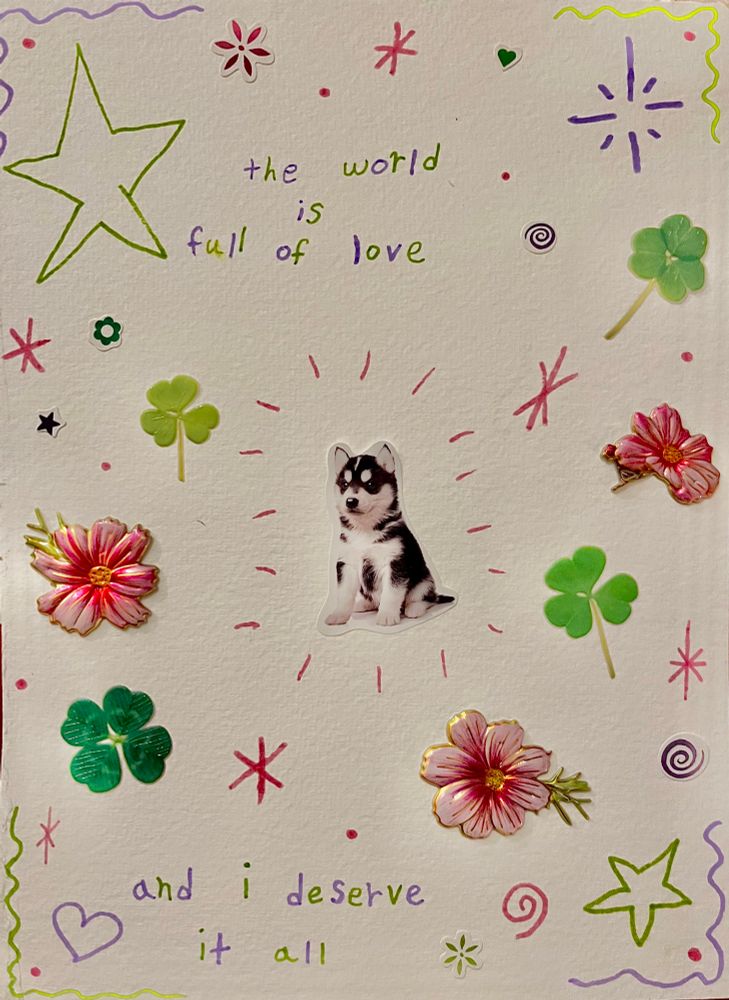 Mixed media sticker and marker collage. In the center is a black and white puppy. It surrounded by green clovers and pink flowers. It reads “the world is full of love and I deserve it all”.