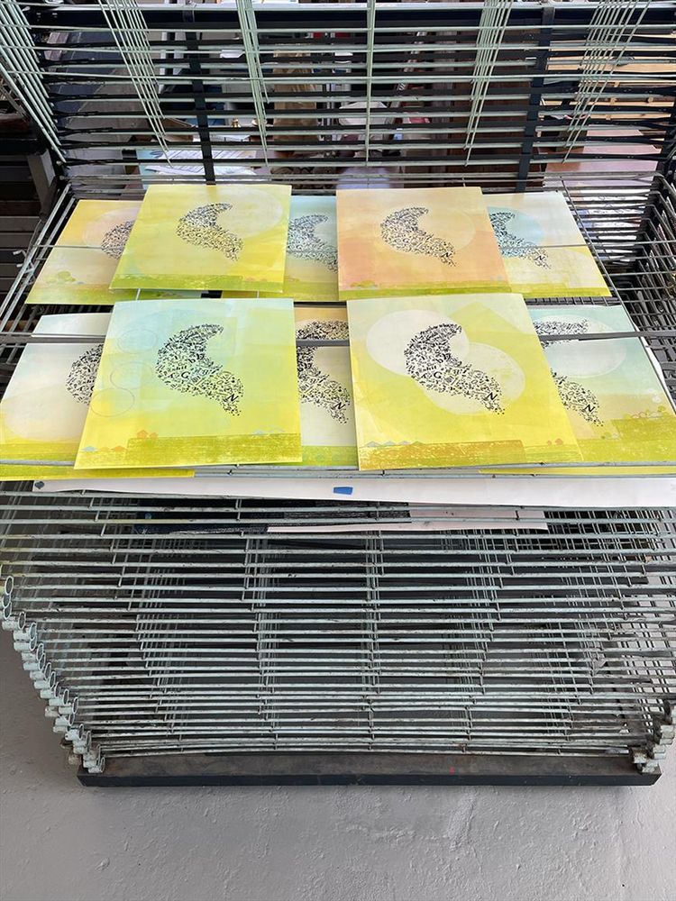 Drying rack with several colorful partially finished prints spread out on it.