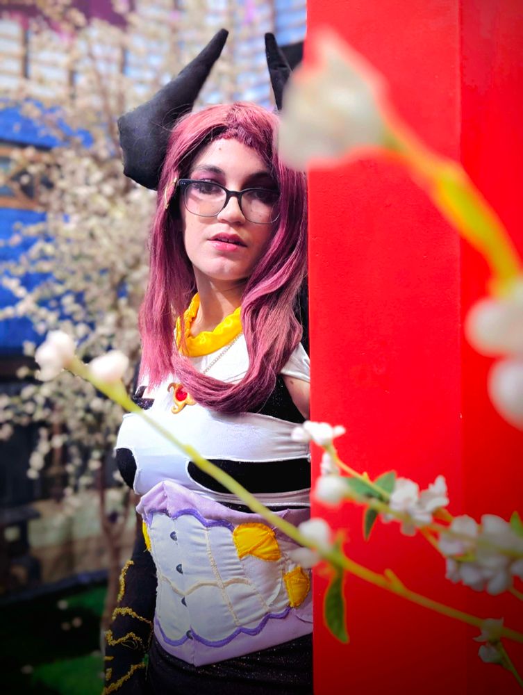 Giwi cosplay in a Sakura photo set, next to a Torii. Looking into the camera w/ Sakura flowers in the foreground. 