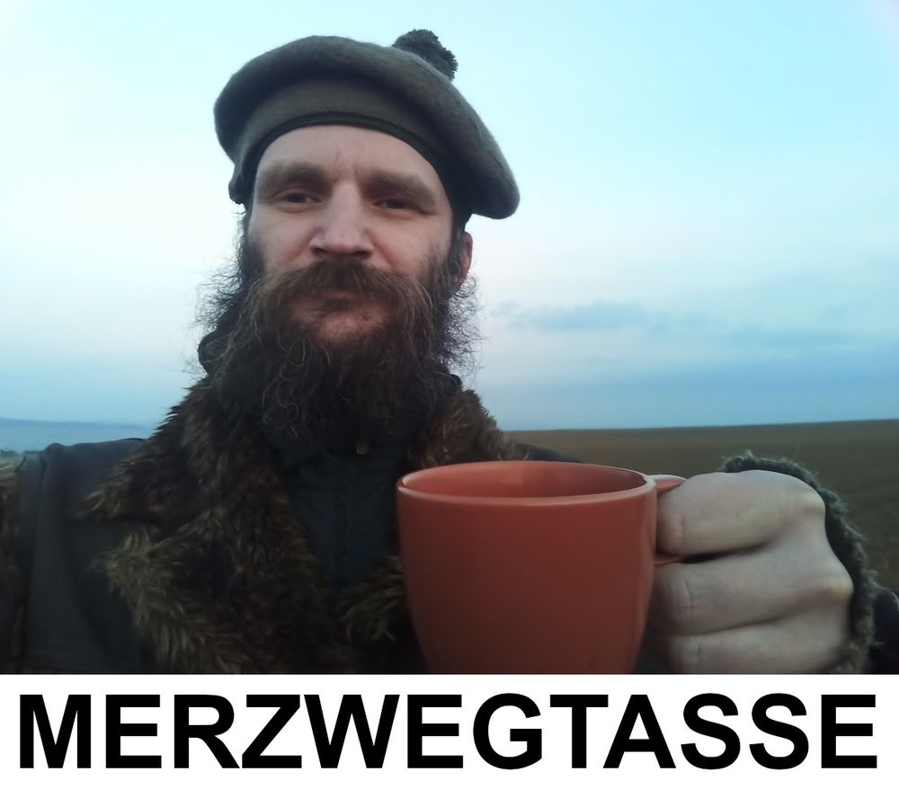 Bärtiger Mann hält eine Tasse ins Bild. Darunter steht in Großbuchstaben "Merzwegtasse".