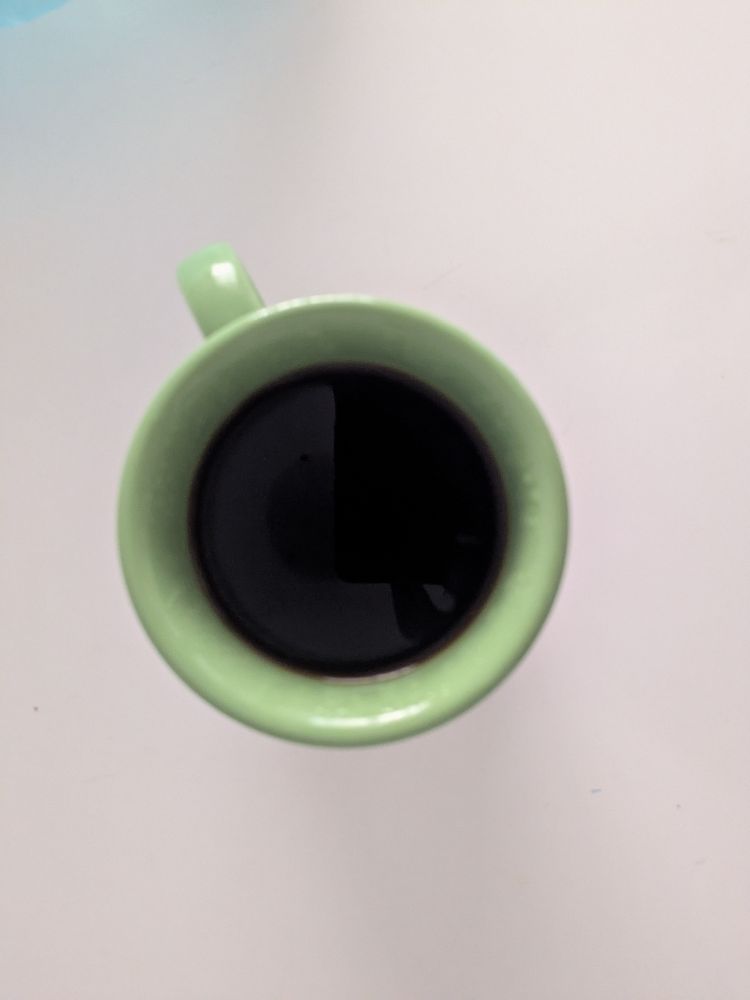 Black filter coffee in a green mug, on a white table. Birds eye view 
