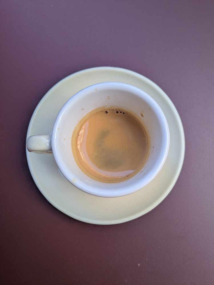 Espresso shot in a white cup (which looks cream in this pic) on a rust coloured table