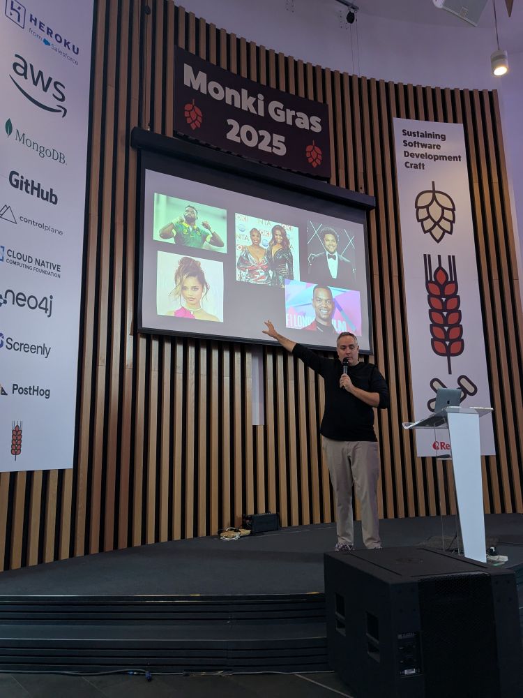 Man on stage showing a slide with a number of (Black) south african celebrities including Trevor noah, johaness, motsi and oti 