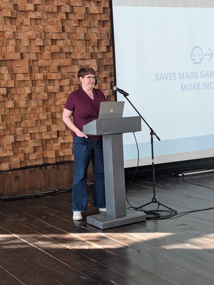A white woman wearing a purple shirt and blue jeans, presenting at a tech conference 