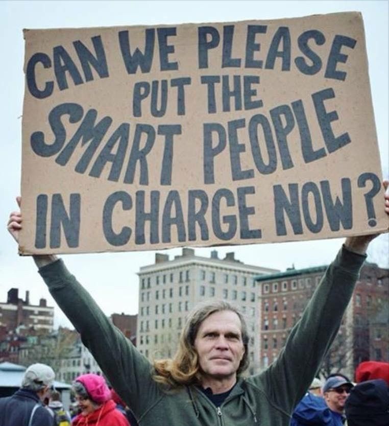 Man holding sign that says Can we please put the smart people in charge now?