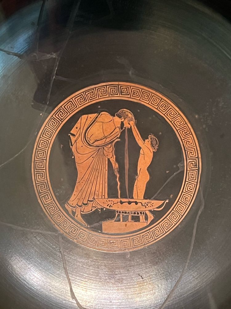 A Ancient Greek drawing of a man throwing up. Painted in red color on black background in a drinking cup