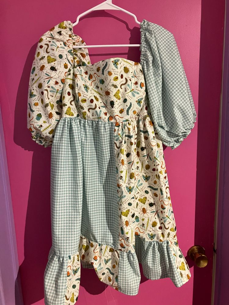 Puff sleeved, tiered dress, in a patchwork of green and white gingham and insects on a white background. 