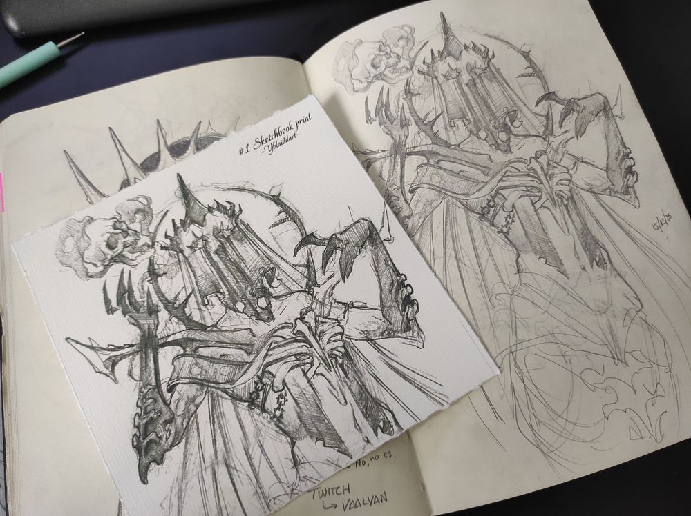 Sobre mi sketchbook abierto se aprecia el mismo boceto, el original y la version impresa en un formato cuadrado de un boceto de una nigromante.