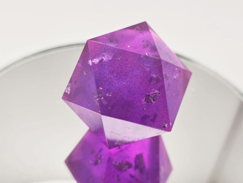An absolutely gorgeous chonky d20 blank that is pink/purple with blue mica powder and bits of silver foil inside.