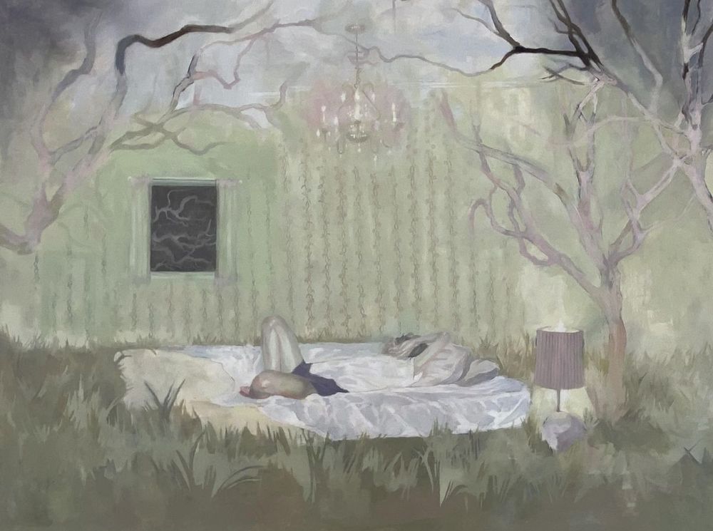 A  painting of a person reclined on a mattress in a surreal, dreamlike outdoor/indoor scene. Maevis Chamberlain, 𝘋𝘳𝘦𝘢𝘮𝘪𝘯𝘨 𝘰𝘯 𝘵𝘩𝘦 𝘍𝘰𝘳𝘦𝘴𝘵 𝘍𝘭𝘰𝘰𝘳, 2025, Oil on Canvas. Photo courtesy of the artist.