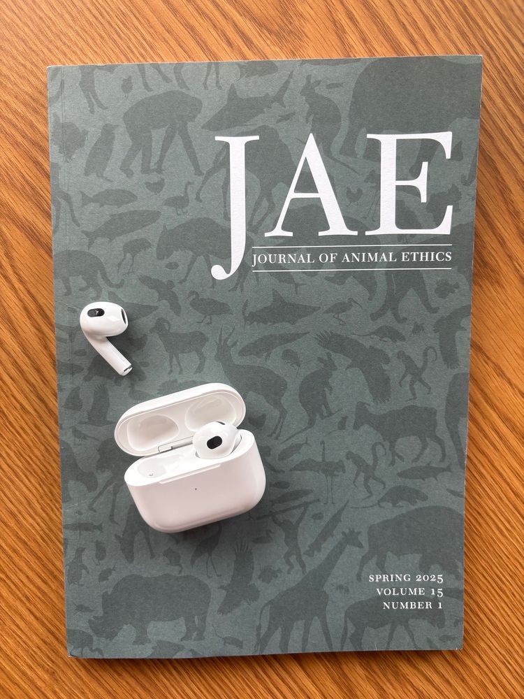 Issue of Journal of Animal Ethics on a wooden table, with an open headphone case to indicate listening to a podcast