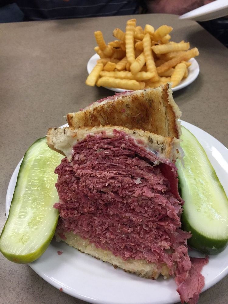 picture of a Slyman's Rueben as bug as your head with a split kosher dill pickle and a plate of crinkle cut fries